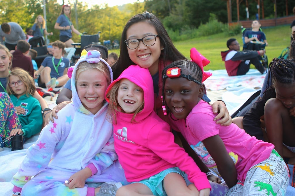 Three happy campers with a volunteer outside at a pajama party at Double H Ranch, the SeriousFun camp in New York