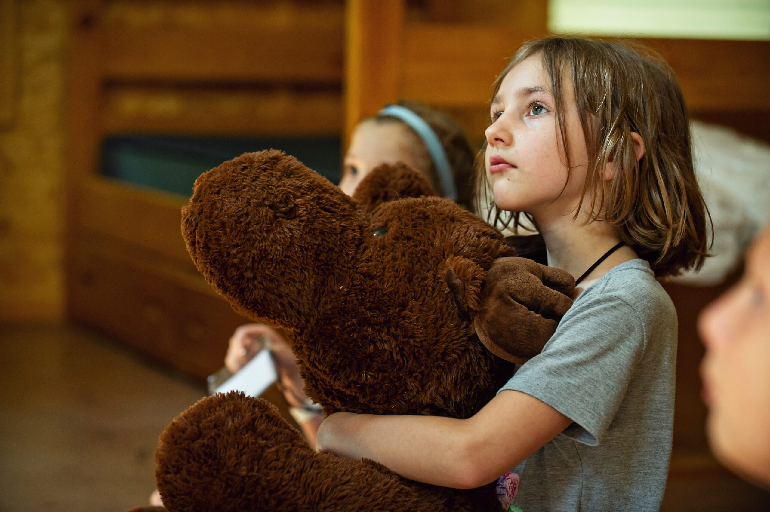 A camper hugging a giant teddy bear listening intently during Cabin Chat