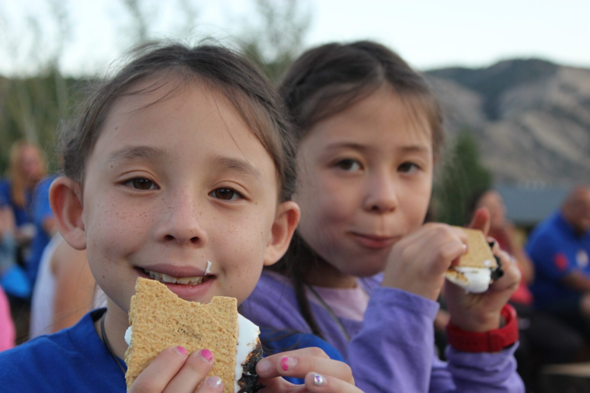 Two girls smile at the camera while snacking on s'mores